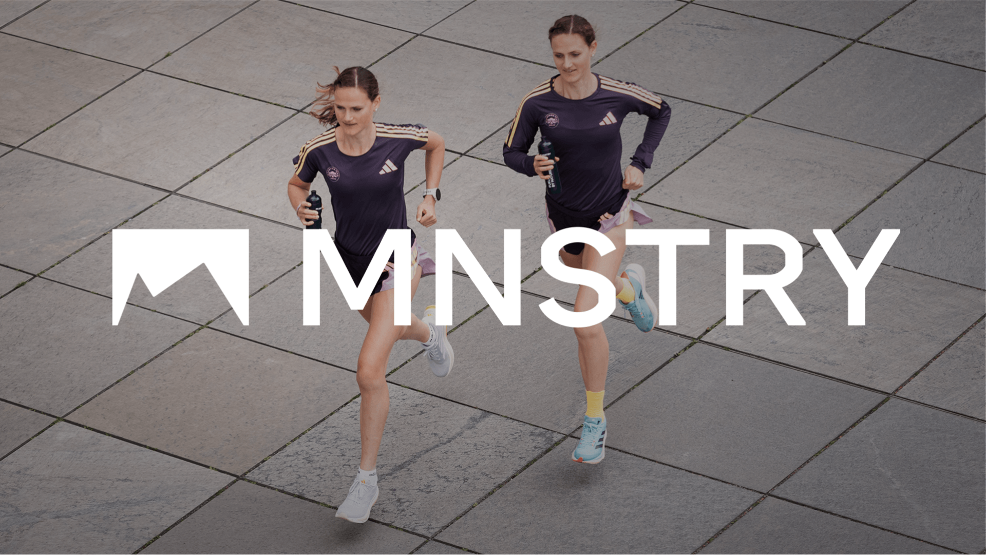 Deborah and Rabea Schöneborn are walking across a square with bottles in their hands. The MNSTRY logo and lettering in white are overlayed on top.