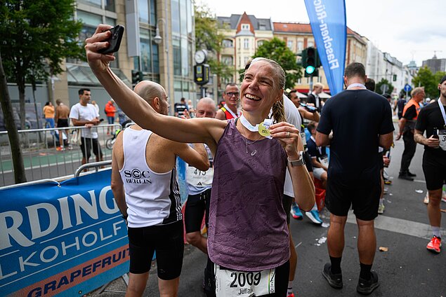 Frau macht nach dem Rennen Selfie mit Medaille