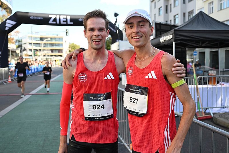 J. Motschmann und S. Hendel stehen nach Zieleinlauf glücklich nebeneinander; Ziel im Hintergrund.