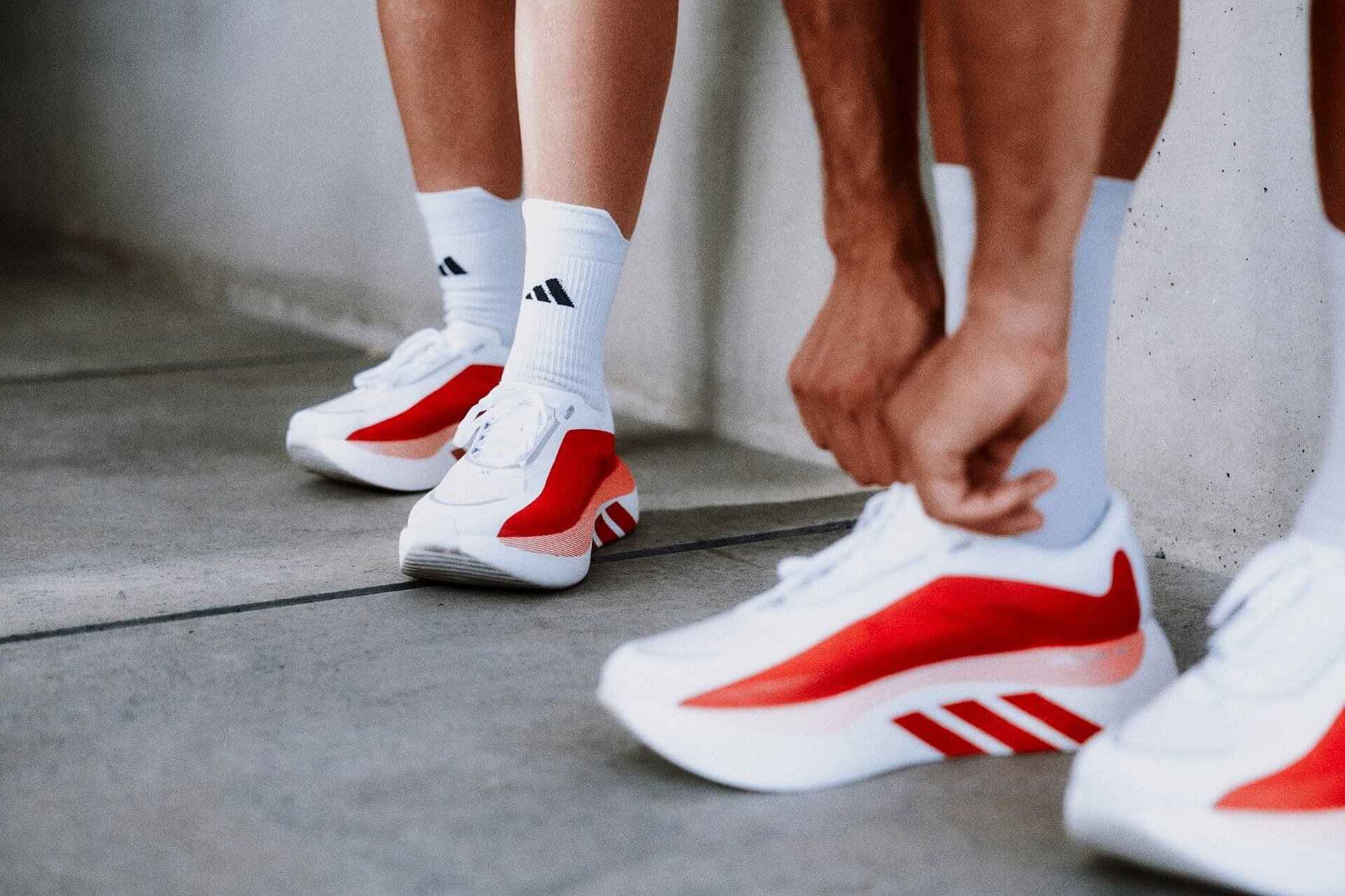 Four feet in white adidas running shoes with red accents.