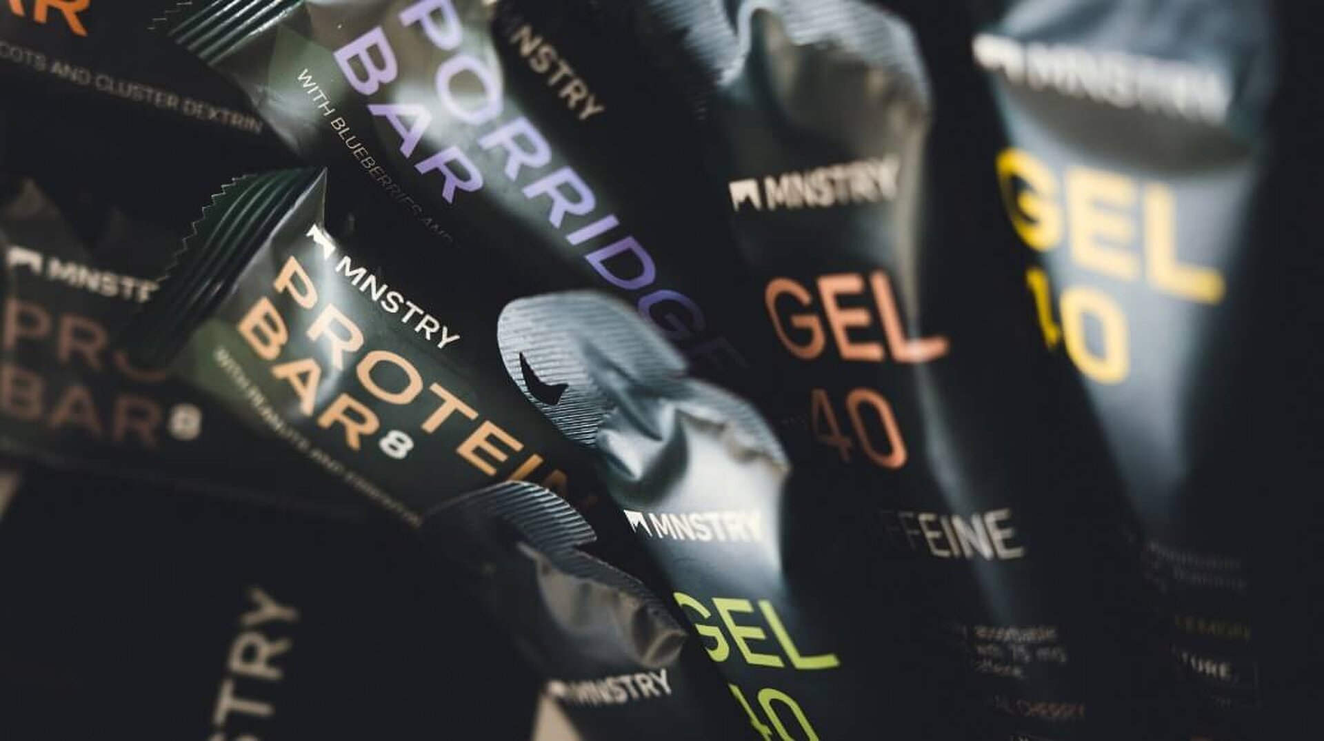 Close-ups of various MNSTRY products, including protein bars, porridge bars, and gels.