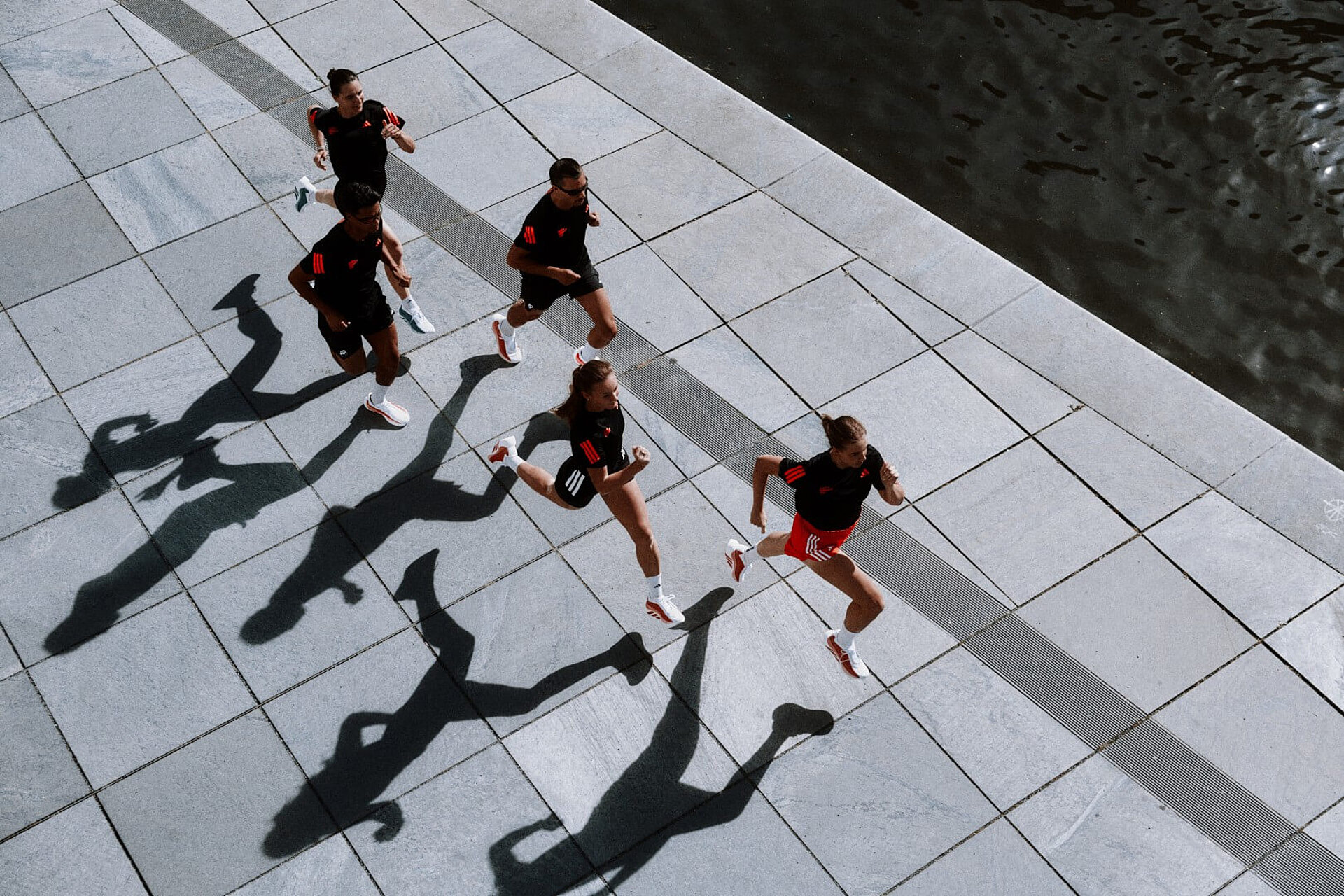 A bird's-eye view of five joggers wearing the same black-and-orange outfits and white-and-red shoes.