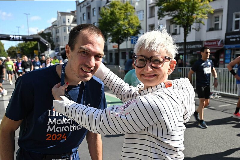 Christine hängt Lauffreund Sascha die Medaille von die Generalprobe um; Beide lächeln glücklich.