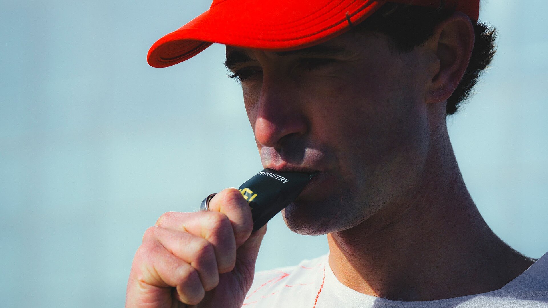 A man wearing a bright red cap is eating an MNSTRY gel.
